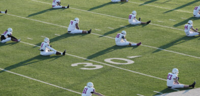 Seated football players engaging in pre-game stretching on the field